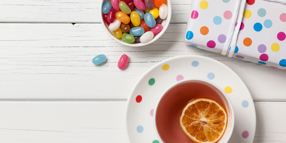 Gift box, cup of tea and colorful candies on white wooden background