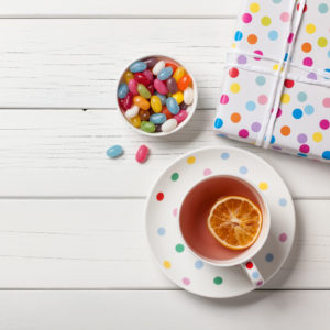 Gift box, cup of tea and colorful candies on white wooden background