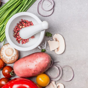 Various vegetables and spices cooking ingredients with red paprika , Mortar and Pestle and wooden spoon on stone slate background, top view, banner. Healthy eating  concept.